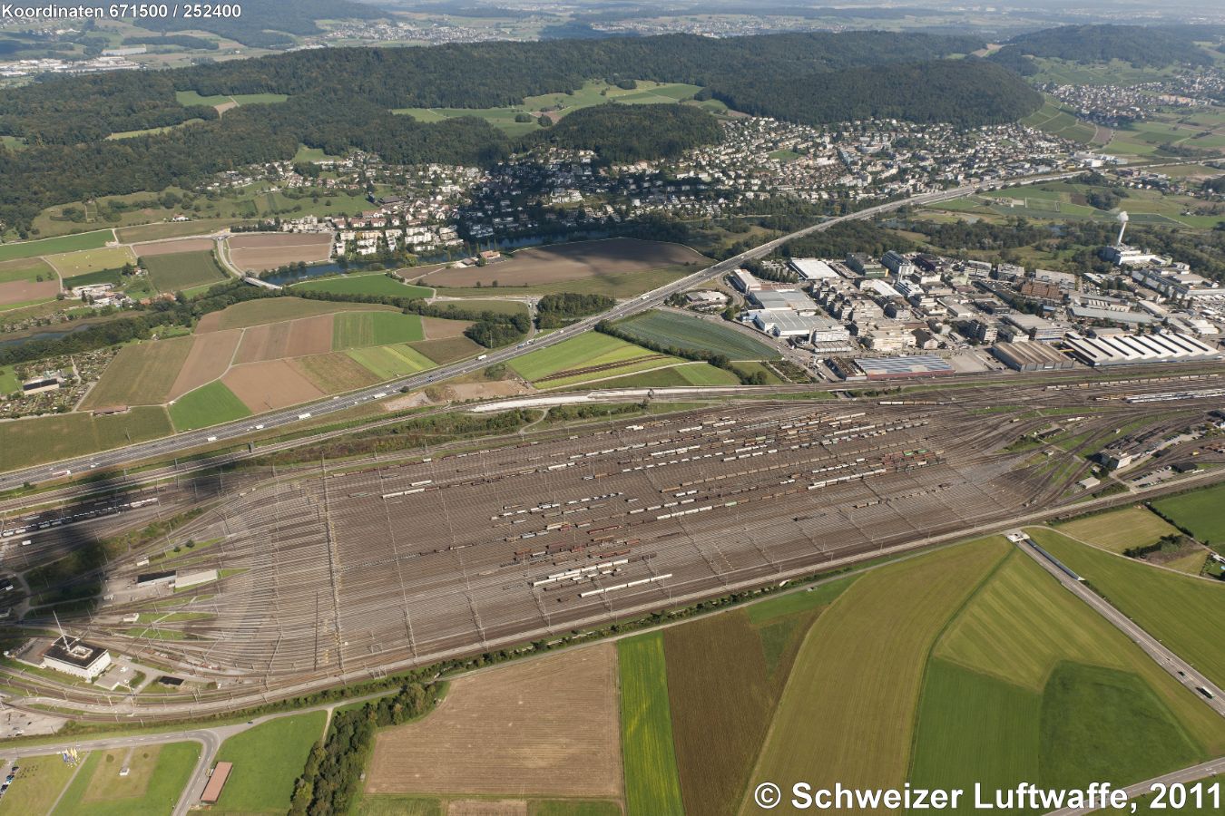 Rangierbahnhof Limmattal (Position: 2'671'495.94, 1'252'466.23). Blick nach NE (obere Mitte) zur Gemeinde Oetwil an der Limmat; gegen rechte obere Bildecke: Geroldswil. Zwischen Autobahn A1 und Bahngeleise: Industriegebiet Moosmatt. Hügelzug: Lägern, dahinter das Furt-Tal